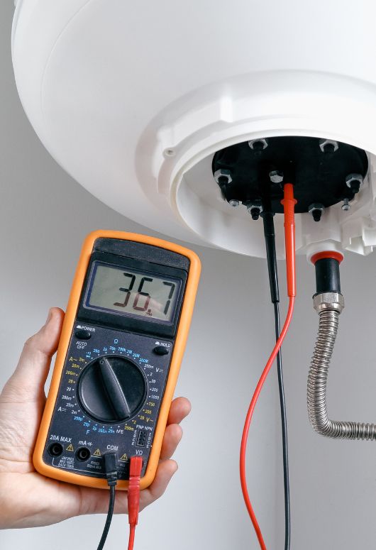 A person uses an electronic meter to check the temperature of a water heater, representing appliance repair services in San Jose, CA.