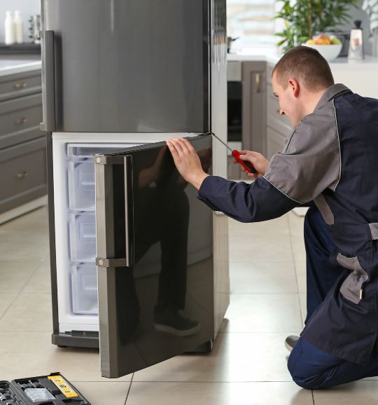 A man works on a refrigerator in a kitchen, highlighting appliance repair services available in San Jose, CA.