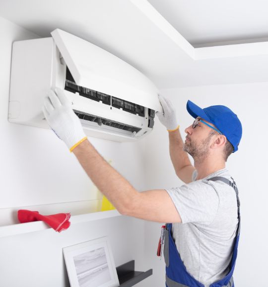 A man wearing overalls and gloves fixes an air conditioner, showcasing heating and cooling repair services in San Jose, CA.