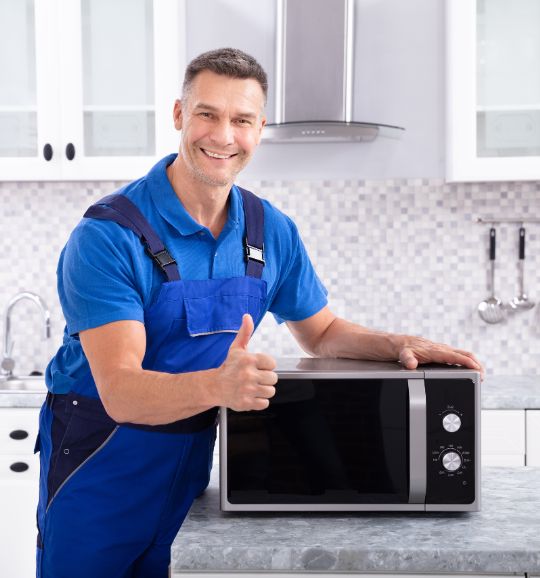 A man in overalls grips a microwave oven, illustrating commercial appliance repair services available in San Jose, CA.