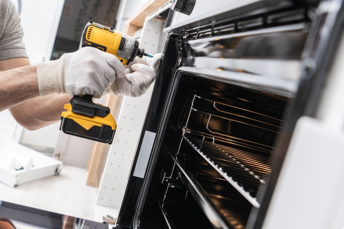 A man repairs an oven using a drill, demonstrating his skills in home maintenance and appliance repair. 
