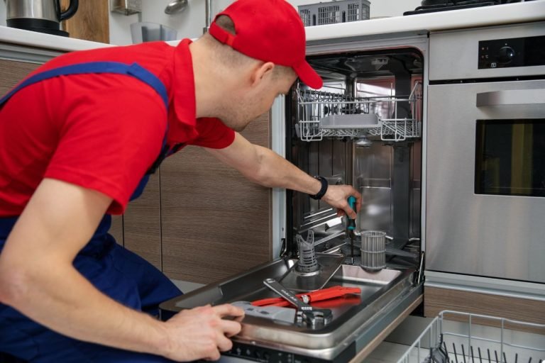 A man dressed in red is working on a dishwasher, demonstrating his expertise in appliance repair.