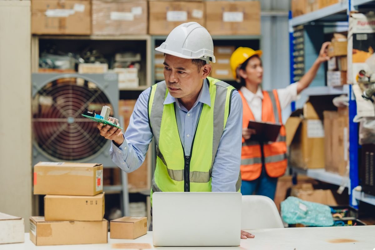 A construction worker in a hard hat and safety vest is using a laptop to complete his tasks.